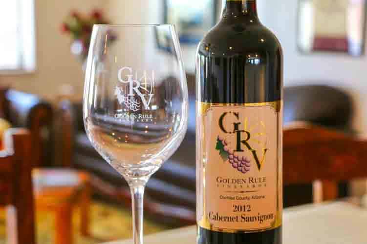 An empty wine glass beside a bottle of wine. The wine bottle label says "GRV: Golden Rule Vineyards" and "2012 Cabernet Sauvignon."
